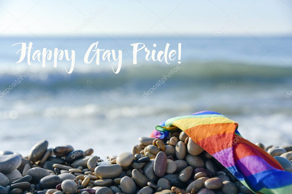 rainbow flag and text happy gay pride on the beach