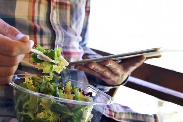 man eating a prepared salad and using a tablet
