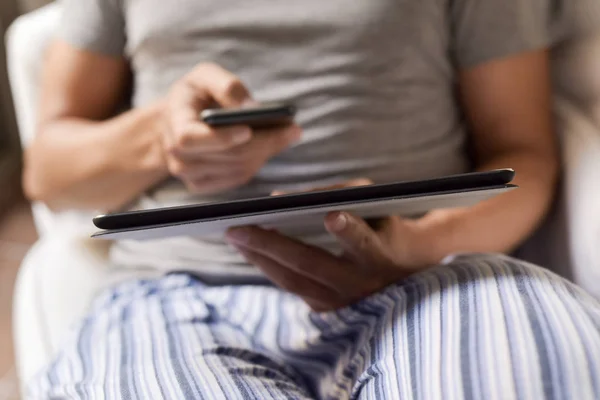 Man in pyjama met behulp van een smartphone en een tablet — Stockfoto