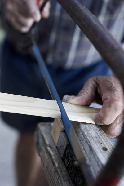 Viejo hombre aserrando una tira de madera con una sierra de mano — Foto de Stock