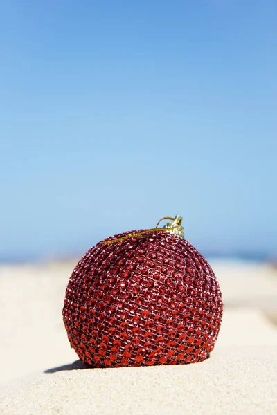 Bola de Natal vermelho na areia de uma praia — Fotografia de Stock