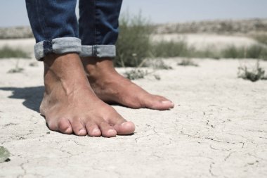 bare feet of a man on a cracked dry soil clipart