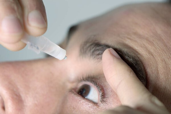 man applying eye drops to his eyes