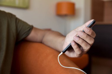 içine takılı bir kablo ile smpartphone kullanan adam