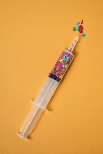 Confetti in a syringe on an orange background — Stock Photo, Image