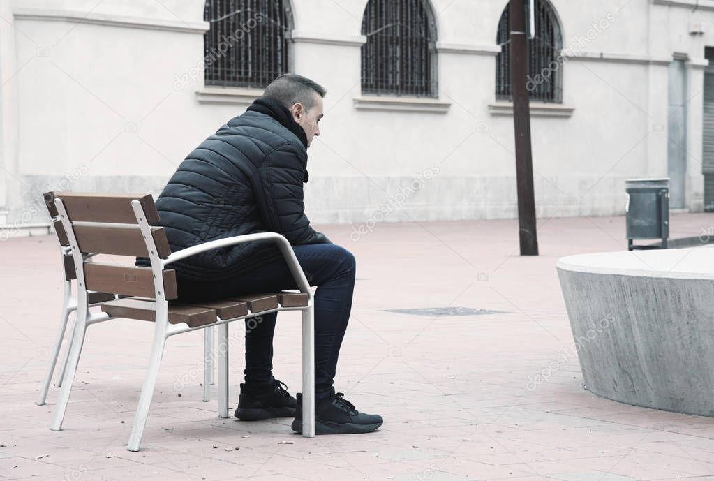 sad man sitting in a bench in the street