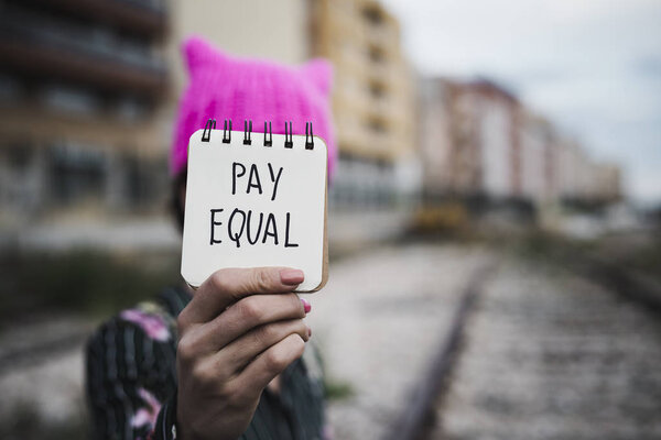 woman with a pink hat and the text pay equal