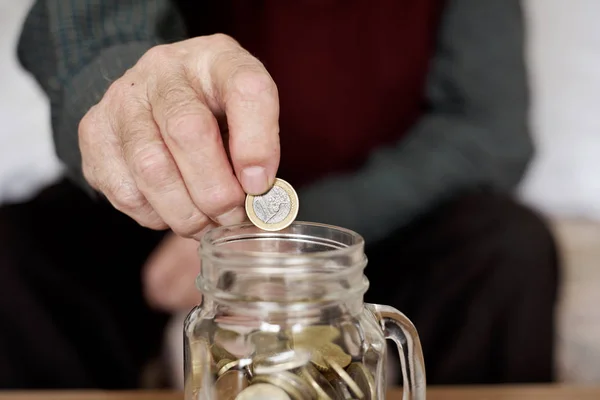 Viejo hombre ahorrando una moneda de un euro en una olla de cristal — Foto de Stock