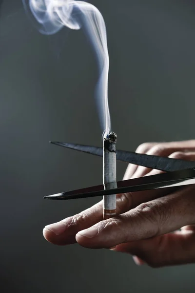 Homem cortando um cigarro aceso com tesoura — Fotografia de Stock