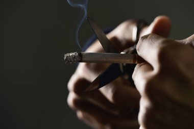 man cutting a lit cigarette with scissors clipart