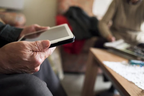 Homem velho usando um tablet e mulher velha leitura — Fotografia de Stock