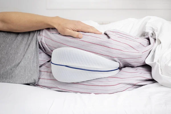 Homem na cama usando uma almofada anatômica da perna — Fotografia de Stock