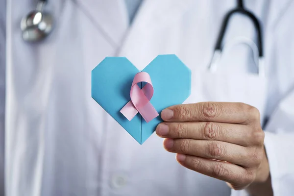 Médico com um coração e uma fita rosa na mão — Fotografia de Stock