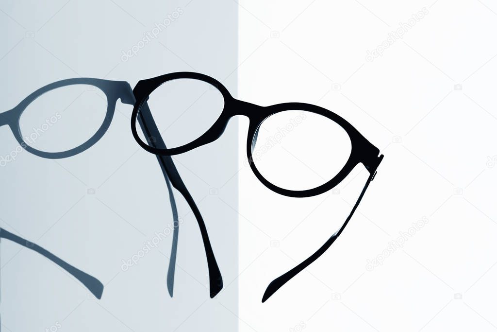 closeup of a pair of black eyeglasses on a reflecting surface against a white background