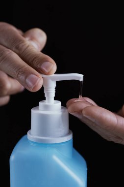 Kafkasyalı bir adamın mavi bir şişedeki el dezenfektanı ile ellerini dezenfekte etmesi.