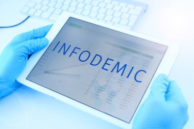closeup of a doctor man, wearing blue surgical gloves, having a digital tablet in his hands with the word infodemic in its screen clipart