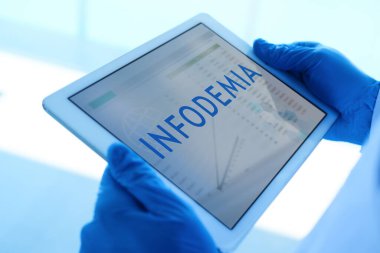 closeup of a doctor man, wearing blue surgical gloves, having a digital tablet in his hands with the word infodemia, infodemic written in spanish, in its screen clipart