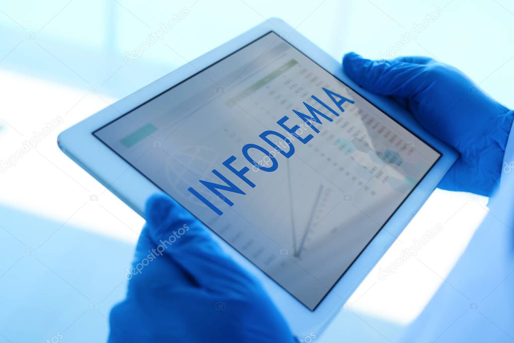 closeup of a doctor man, wearing blue surgical gloves, having a digital tablet in his hands with the word infodemia, infodemic written in spanish, in its screen