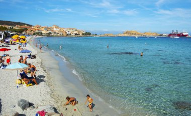 Ile-Rousse, Fransa - 22 Eylül 2018: Ile-Rousse, Corsica, Fransa ve Ile de la Pietra adasının ana plajlarında insanlar ve sağdaki feribot limanında bir gemi