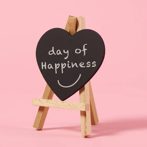 一个黑色的特写 一个心形的标志 上面写着幸福的文字日 放在木制的画架上 粉红的背景上 — 图库照片