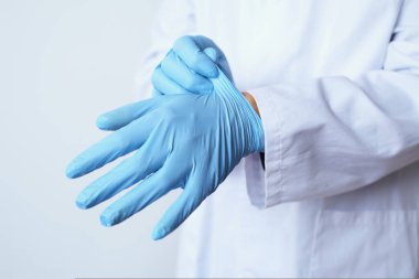 Beyaz önlüklü beyaz bir doktor, mavi bir çift ameliyat eldiveni giyiyor.
