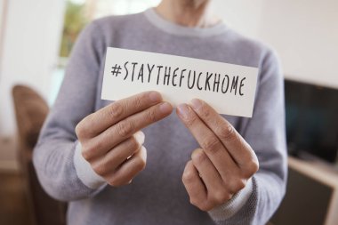 closeup of a man indoors showing the message #staythefuckhome written in a piece of paper, to alert of the need to stay as a measure to stop the spreading of the covid-19 clipart