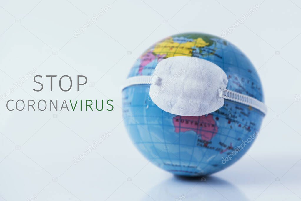 closeup of a terrestrial globe with a protective mask and the text stop coronavirus against an off-white background
