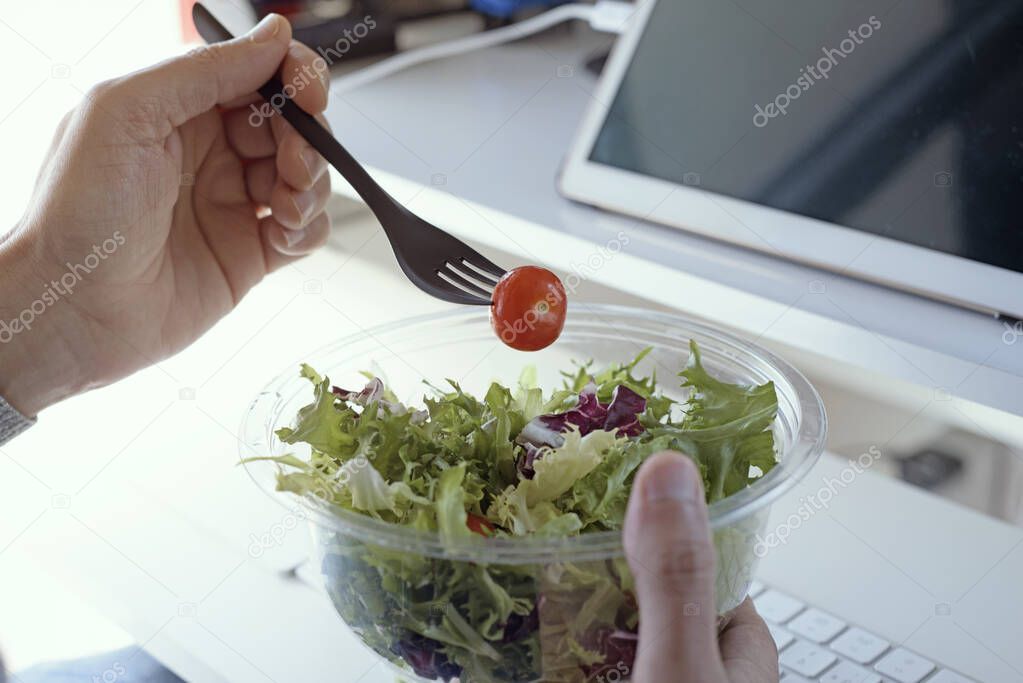 closeup of a young caucasian man eating salad from a plastic container sitting at his desk