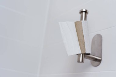 closeup of a roll of toilet paper with a last piece o paper hanging from the toilet paper holder in a tiled bathroom clipart