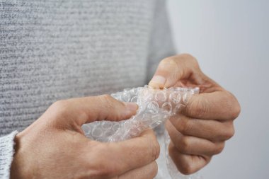 Kafkasyalı genç bir adamın yakın çekimi, günlük giysiler giymiş, baloncuklu ambalajın baloncuklarını patlatıyor.