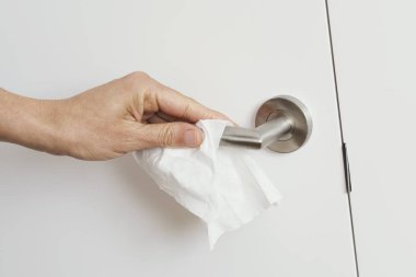 Beyaz bir adamın dezenfekte beziyle kapı kolunu temizlediği yakın plan.