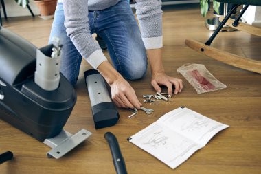 a caucasian man assembling the different pieces of a stationary bicycle in the living room of his house clipart