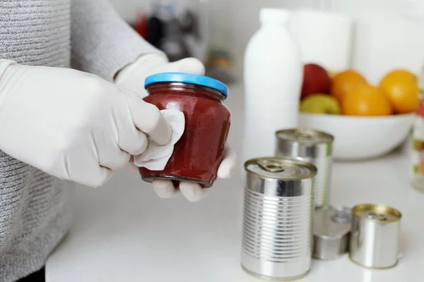 closeup of a man in the kitchen, wearing latex gloves, cleaning food cans and jars, freshly purchased, with a disinfecting wipe