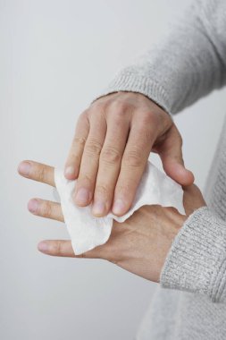 Kafkasyalı bir adamın yakın çekimi, günlük soluk gri bir kazak giyiyor, ellerini dezenfekte beziyle temizliyor.