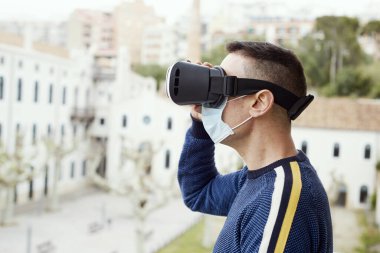 closeup of a caucasian man, wearing a surgical mask, using a virtual reality headset outdoors,  in a balcony or a private terrace clipart