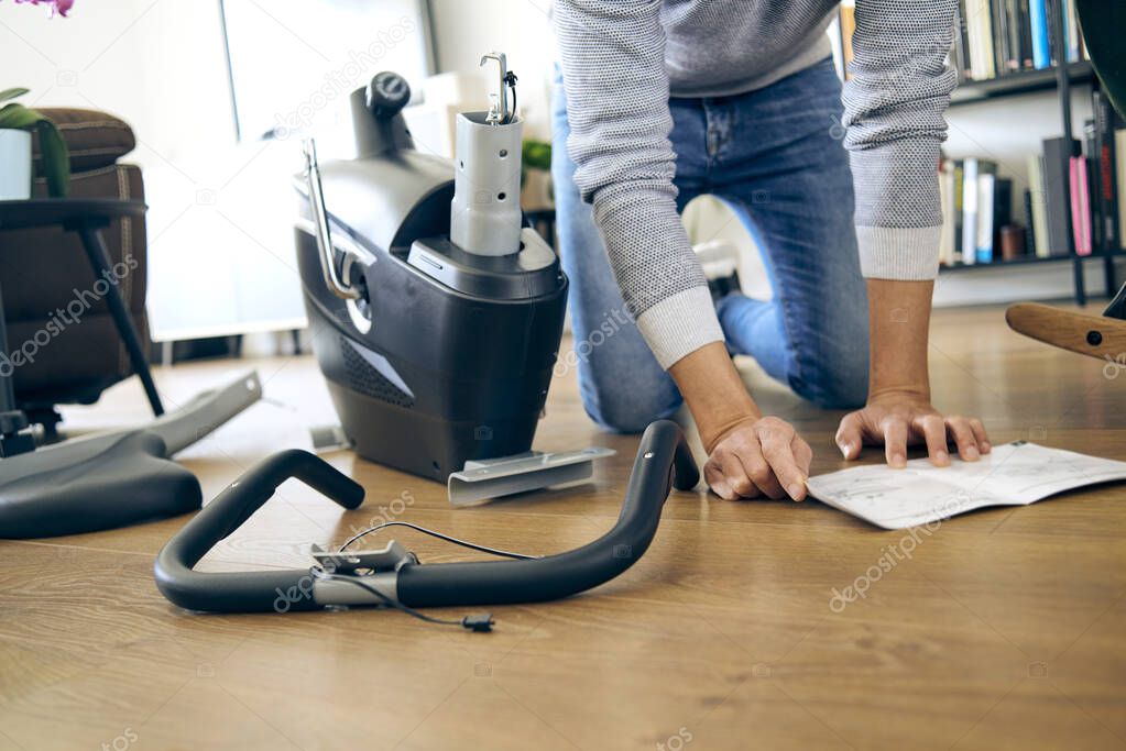 a caucasian man assembling the different pieces of a stationary bicycle in the living room of his house