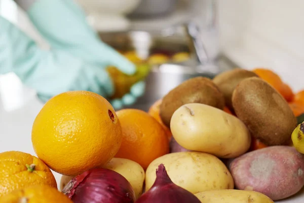 closeup of a man in the kitchen, wearing gloves, washing some fruits and vegetables freshly purchased, on the sink with water and food sanitizer