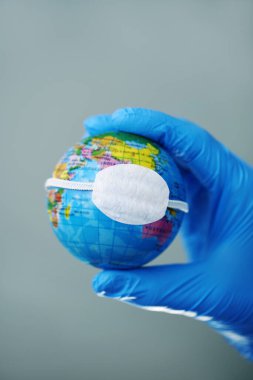 Eldiven takan bir doktor koruyucu bir maskeyle karasal bir küreyi tutarken küresel koronavirüs salgınını ya da gezegendeki hava kirliliğini resmediyor.