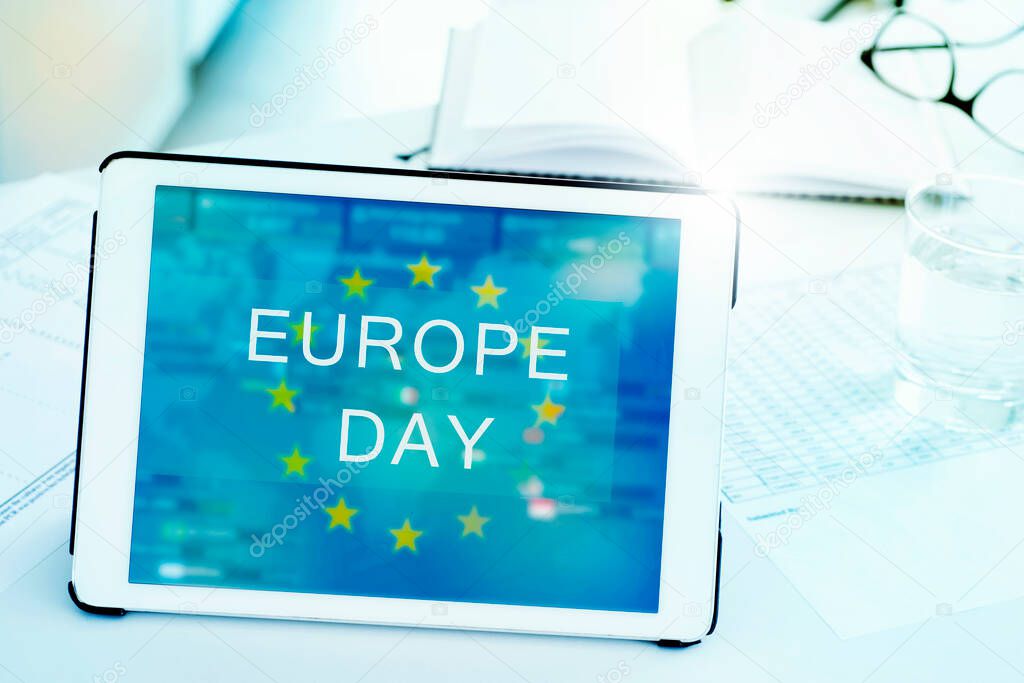 closeup of a digital tablet, with the text Europe Day and the flag of the European Union in its screen, on a white desk