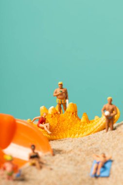 Bazı farklı minyatür insanlar mayo giyip plajın kumsalında ya da deniz yıldızının yanında, üzerinde boş bir alan olan mavi bir arka plana yaslanıyorlar.