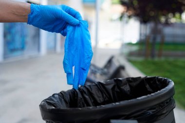 Caddedeki çöp kutusuna kullanılmış mavi lateks eldiven atan bir adamın yakın çekimi.