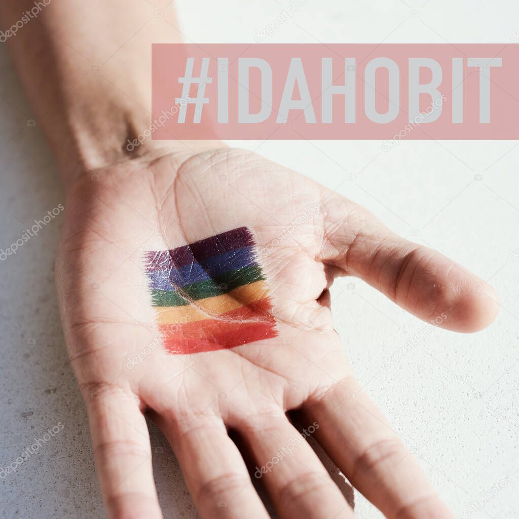 closeup of a rainbow flag in the palm of the hand of a young person, and the text IDAHOBIT, for International Day Against Homophobia, Biphobia, Interphobia and Transphobia