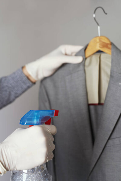 closeup of a man, wearing latex gloves, disinfecting a sport jacket hanging on a clothes hanger by spraying a disinfectant from a bottle