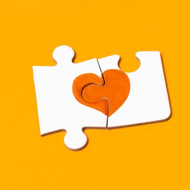Turuncu bir kalp oluşturan bir yapbozun iki parçasına yakın çekim, turuncu arka planda çoklu sklerozdan etkilenen insanları desteklemek için.