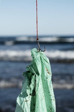 Kullanılmış yeşil plastik bir torbaya yakın plan, balık oltasında, okyanusta yeni avlanmış.