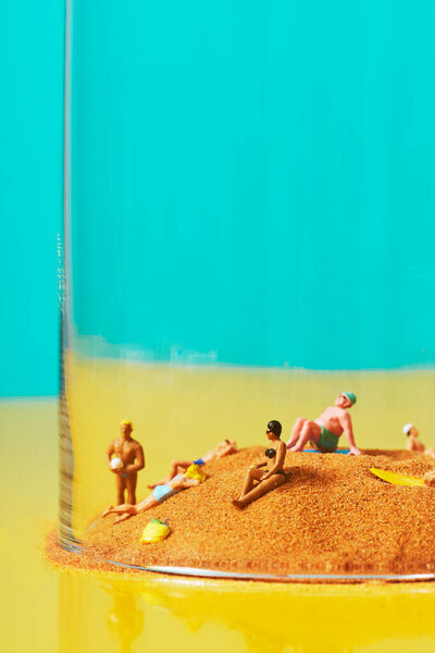 some miniature people wearing swimsuit relaxing on the sand in a bell jar, symbolizing different ideas, such as the greenhouse effect or the protection on the beach in the post-covid-19 situation