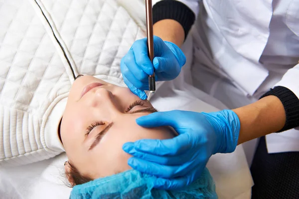 Assistente de maquiagem permanente faz procedimento de correção de sobrancelha . — Fotografia de Stock