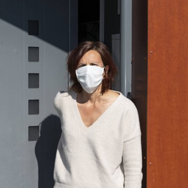 Evde, kapının önünde maske takan bir kadın.