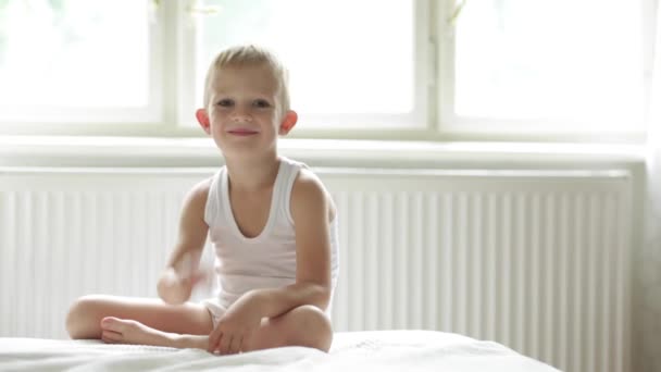 幸せなリラックスした笑顔の子は白いベッドの上 ok の標識を表示します。 — ストック動画