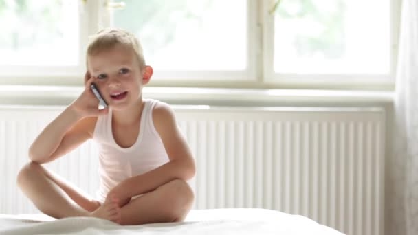 Щаслива дитина розмовляє на стільниці, смартфон, сидить на ліжку — стокове відео